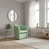 A mint green armchair is placed in a room with a round mirror on the wall, a small side table with a plant, and a wooden media console with plants and books. Produktbild-Vorschau