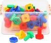 A clear, well-lit studio shot of a plastic toy construction set, featuring colorful nuts, bolts, and geometric shapes, contained within a transparent plastic bin. Some pieces are scattered outside the bin in the foreground. Anteprima dell’immagine prodotto