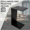 A black C-shaped side table is shown in a living room setting with a blurred background of a sofa and coffee table. Text overlays highlight its design. Produktbild-Vorschau