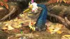 A creature with a blue, scaled body and a yellow beak, adorned with flowers, stands on a forest floor covered in leaves. Produktbild-Vorschau
