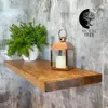A wooden shelf with a plant and a lantern on it, mounted on a textured wall. Produktbild-Vorschau