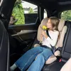 A young girl sits in a car seat in the back seat of a car, holding a yellow flower. Produktbild-Vorschau