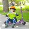 A young boy wearing protective gear sits on a purple scooter and drinks from a water bottle in a park. Náhľad obrázku produktu