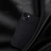 A black leather-textured phone case with a camera cover is placed on a black leather surface. Podgląd zdjęcia produktu
