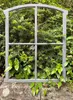 A gray metal window frame is placed in front of lush green foliage and on top of a stone wall. Produktbild-Vorschau