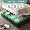 A bed with its storage compartment open, showing folded clothes and storage boxes inside. Produktbild-Vorschau