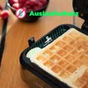 A close-up of a waffle iron with a waffle inside, with raspberries in the background. Produktbild-Vorschau