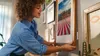 A woman is hanging a framed picture on a wall. Anteprima dell’immagine prodotto