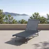 A dark gray chaise lounge is positioned on a tiled patio overlooking a body of water and distant hills.