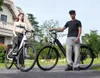 Two people posing with electric bikes in front of a house. Produktbild-Vorschau