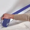 A person's hand is applying blue painter's tape to a wall and trim. The floor is covered with a drop cloth. Anteprima dell’immagine prodotto