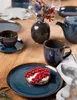 A table setting with plates, cups, a teapot, and a small vase with flowers, featuring a dessert with red currants. Voir les images du produit