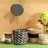 A decorative arrangement of home decor items, including a sunburst mirror, woven baskets, and a candle, displayed against an orange wall and green surface. Voir les images du produit