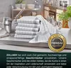 A stack of folded kitchen towels on a countertop with kitchenware in the background. Produktbild-Vorschau