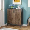 A shoe cabinet with decorative doors is placed in an entryway or hallway, next to a white door and a wall with a framed picture and flowers. Voir les images du produit