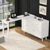 A white L-shaped desk with a rotating extension is set up in a room with a large window and a rug. Produktbild-Vorschau