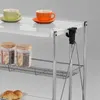 A close-up view of a white rolling cart with chrome accents, displaying two cups and saucers on the top shelf, two jars on the middle shelf, and croissants on a plate on the bottom shelf. Produktbild-Vorschau