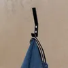 A black coat hook mounted on a beige wall, with a denim jacket hanging on it. Produktbild-Vorschau