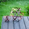 Two decorative garden spheres made of rusted metal sit on a dark wooden table in front of a blurred green lawn. Voir les images du produit