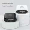 Two digital alarm clocks, one black and one white, are displayed on decorative stands. The black clock is in the foreground, and the white clock is slightly behind and to the right. Both clocks have illuminated displays showing the time and temperature. Produktbild-Vorschau