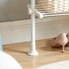 Close-up of the base of a white telescopic clothes rack with a basket on the shelf above, and a pair of beige high heels on the wooden floor. Produktbild-Vorschau