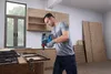 A man is using a power drill to work on a metal frame in a workshop. Produktbild-Vorschau