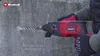 A person is using a red and black rotary hammer drill to drill into a concrete wall. Náhled obrázku produktu