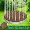 A circular outdoor shower with water spraying upwards, set on a green lawn with some flowers and bushes in the background. Náhled obrázku produktu