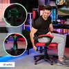 A man is sitting in a red and black gaming chair in a room with colorful lighting. Produktbild-Vorschau