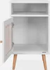 An open white nightstand with a cane door detail and wooden legs, shown against a white background. Produktbild-Vorschau