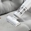 A white handheld vacuum cleaner is shown cleaning a gray fabric surface, likely a sofa or chair. Small debris is visible on the surface being cleaned. Produktbild-Vorschau