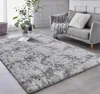 A living room scene with a gray shaggy rug in the foreground and a gray sofa with a throw blanket and pillow in the background. Náhled obrázku produktu
