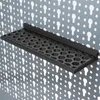 A black shelf with a hexagonal grid pattern is mounted on a pegboard with keyhole slots. Produktbild-Vorschau