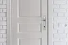 A close-up view of a white door with a silver door handle and a white brick wall next to it. Anteprima dell’immagine prodotto