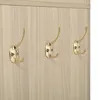 A close-up view of three gold-colored coat hooks mounted on a light wood-grain surface. Podgląd zdjęcia produktu