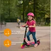 A young girl riding a pink electric scooter in a park. Anteprima dell’immagine prodotto