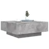 A square coffee table with a concrete-like finish is shown against a white background. A small potted plant and a white cup and saucer are placed on top of the table. Produktbild-Vorschau