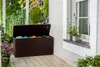 A brown storage box with its lid open, placed on a wooden porch next to a window with plants. Podgląd zdjęcia produktu
