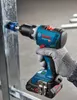 A hand wearing a glove is using a Bosch cordless drill to drill into a metal beam. Náhled obrázku produktu