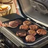 Burgers are being grilled on an electric grill, with a person holding a plate of toppings in the background. Voir les images du produit