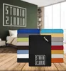 A stack of colorful bed sheets is displayed on a wooden table in front of a bedroom scene with a bed and a wall graphic. Produktbild-Vorschau