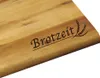 A close-up of a wooden cutting board with text and a wheat graphic engraved on it. Produktbild-Vorschau