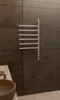 A chrome electric towel warmer with six folding arms is mounted on a dark tiled wall in a bathroom. Náhľad obrázku produktu