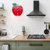 A kitchen scene with a red apple-shaped clock on the wall above a stove and sink. Produktbild-Vorschau