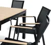 A close-up view of a modern outdoor dining set, featuring a slatted wooden tabletop and black metal chairs with mesh seats and wooden armrests. Produktbild-Vorschau