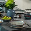 A table setting with plates, bowls, fruit, and a vase of flowers. Produktbild-Vorschau