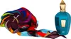 A teal colored perfume bottle with a gold cap and a colorful scarf next to it. Voir les images du produit
