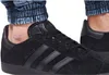 A close-up shot of a person wearing black Adidas Gazelle sneakers. Voir les images du produit