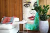 A living room scene with a sofa, a side table, a large painting of a woman's face, and a potted plant. Voir les images du produit