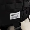 A close-up of a black Alpha Industries backpack with a label showing brand information. Produktbild-Vorschau